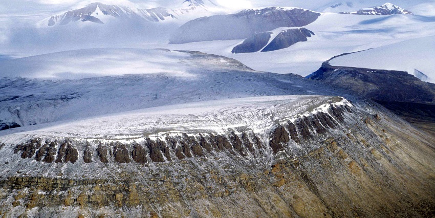 A rugged, mountainous landscape with rocky peaks, patches of snow, and a winding river.