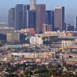 A view of the Downtown Los Angeles skyline, featuring tall skyscrapers, lights, and a clear sky.