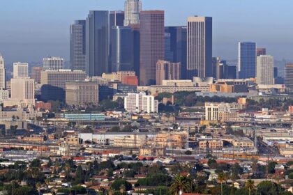 A view of the Downtown Los Angeles skyline, featuring tall skyscrapers, lights, and a clear sky.