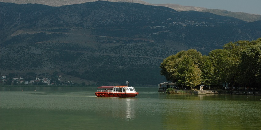 A red and white cruise boat in Lake Loannina with distant buildings and mountains.