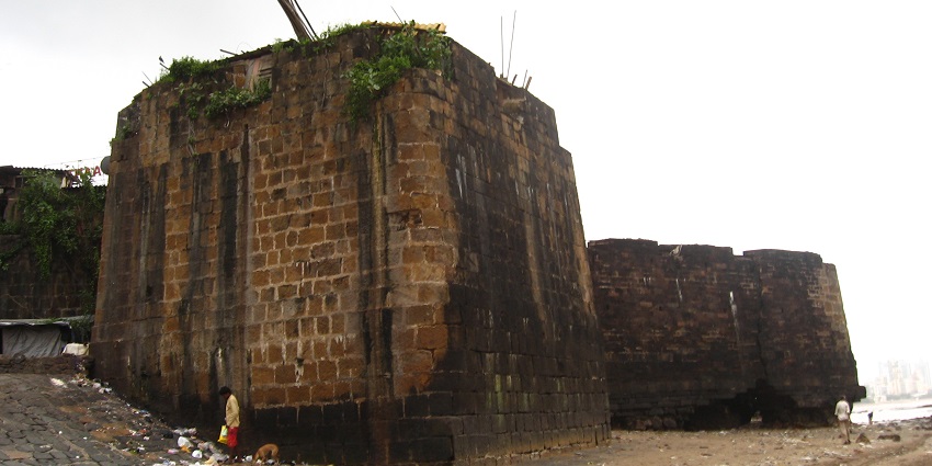 An image of the ruins of Mahim Fort with greenery and the sea in the distance.