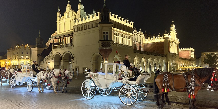 Old town market square in the evening with people riding the carts attached to the horses