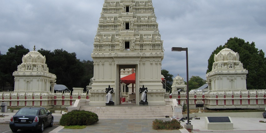An Image of A large Hindu temple with white stone architecture, set against a green hill in Malibu.