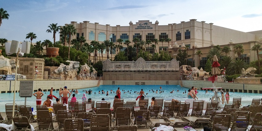 An image of Mandalay Bay Beach's large pool with palm trees, sun loungers, and people enjoying.