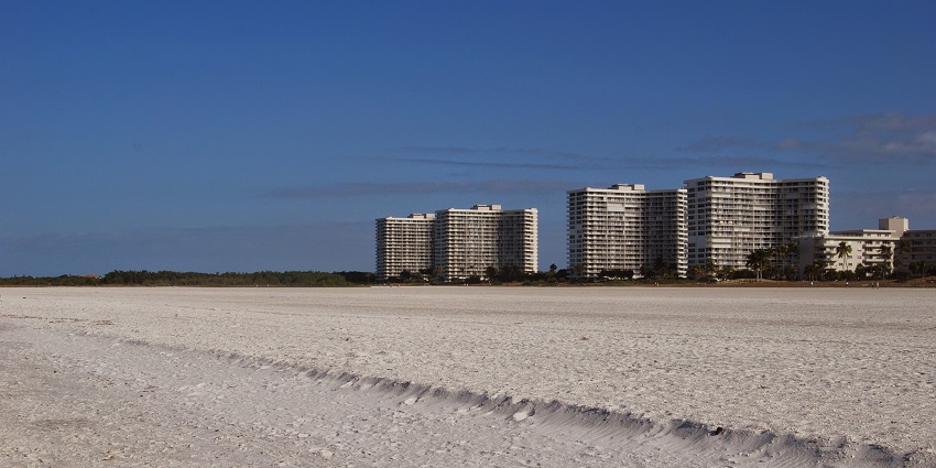An image of Marco Island Beach, Florida, with soft white sand, clear blue waters, and palms