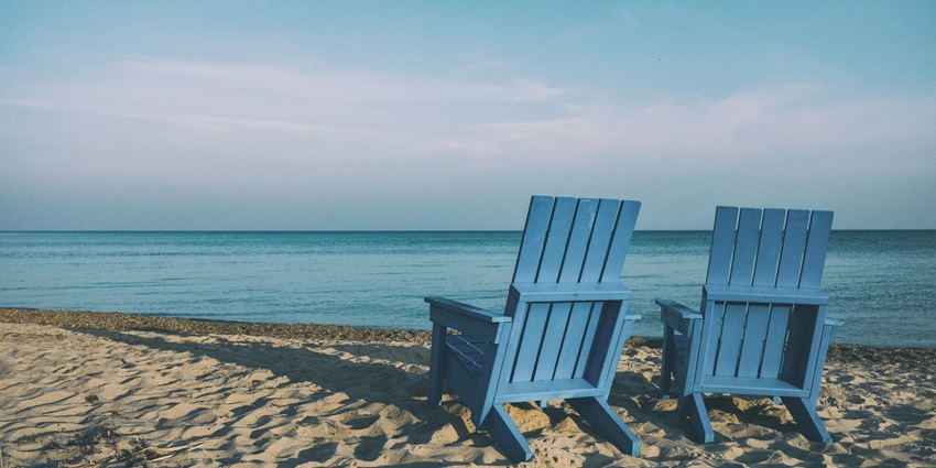 Image of two wooden chair in blue colour in front of the beach and on golden sand for sunbath