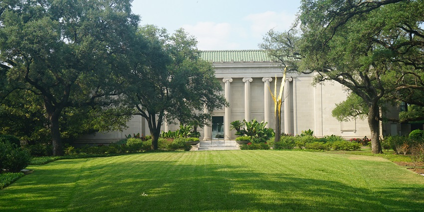 The tall pillared white structure of the Museum of Fine Arts Houston is surrounded by greenery