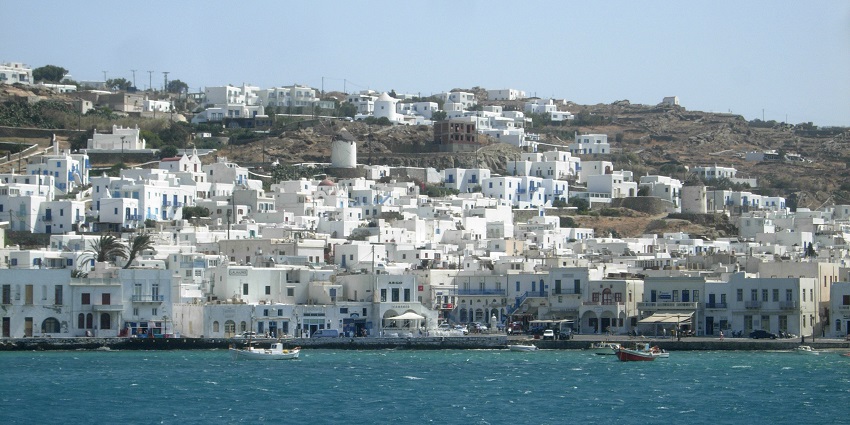 Mykonos town spread over a mountain with boats parked and sailing on the Mykonos water