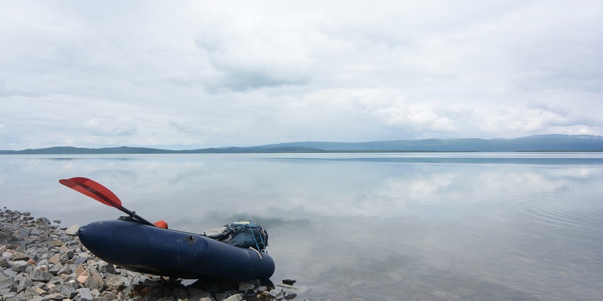 A person paddling a packraft on Naknek Lake, with mountains in view