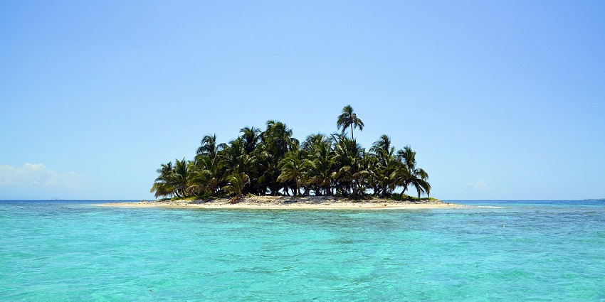 A small, tropical island with palm trees surrounded by turquoise water and a blue sky