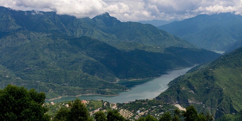 New Tehri reservoir nestled between lush green mountains under cloudy skies in Uttarakhand.