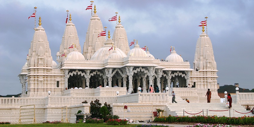 An image of A large Hindu temple in Houston with intricate stone carvings, a dome, and green surroundings