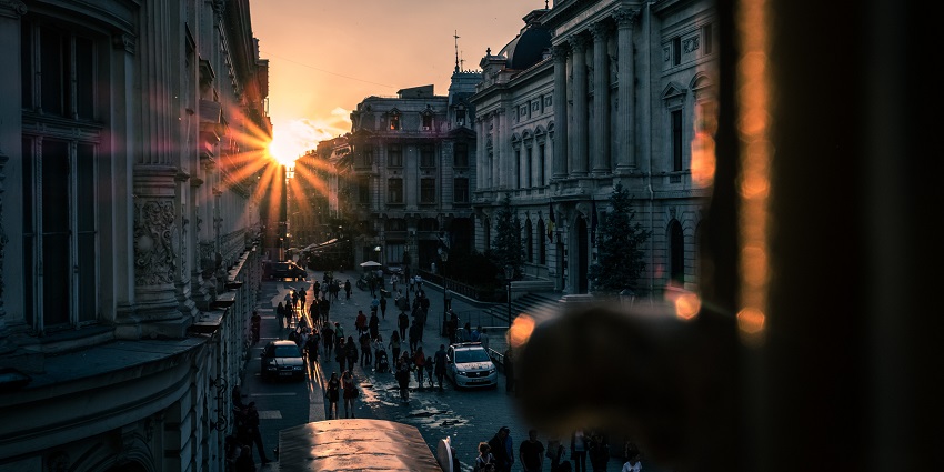 The old town Bucharest with people walking on the street, cops cars and a sunset.