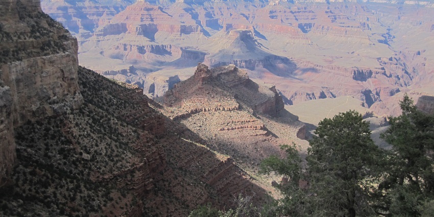 View from a Grand Canyon overlook, showcasing the vast, layered rock formations and rugged terrain.