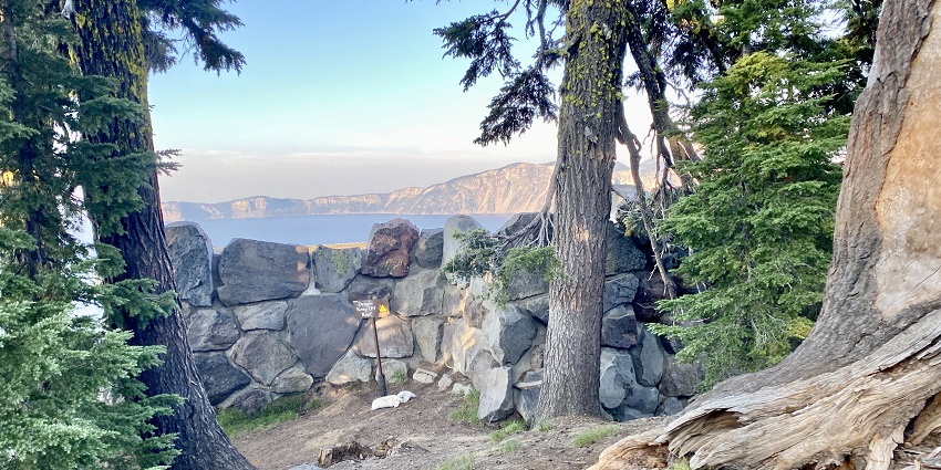An image of the stone wall along the rim of Crater Lake National Park with a forested landscape.
