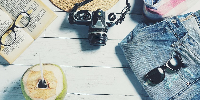 An image of travel things - a hat, a camera, a denim, a sunglasses and more.