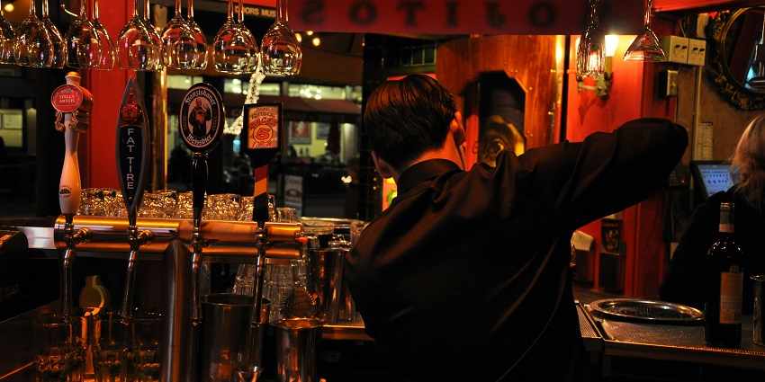 A picture of a person standing at the bar counter, waiting for their cocktail
