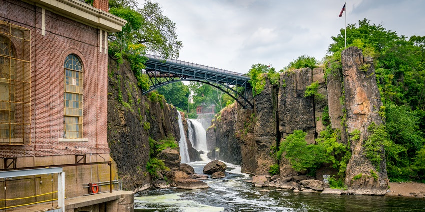 A scenic view of the Paterson Great Falls with water cascading down the cliff into a river