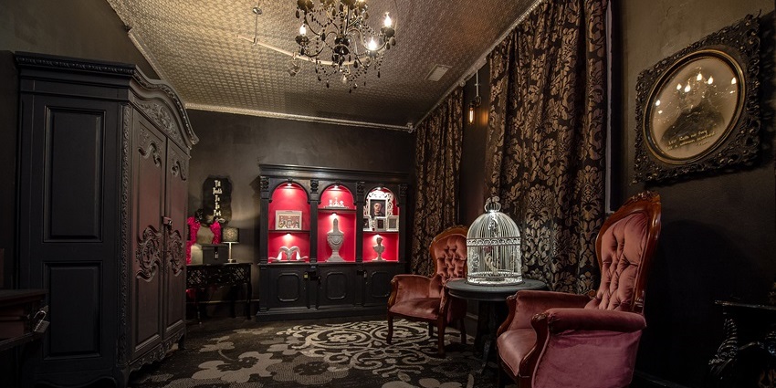A dimly lit room with black and grey interiors, a chandelier and a cage placed on a table