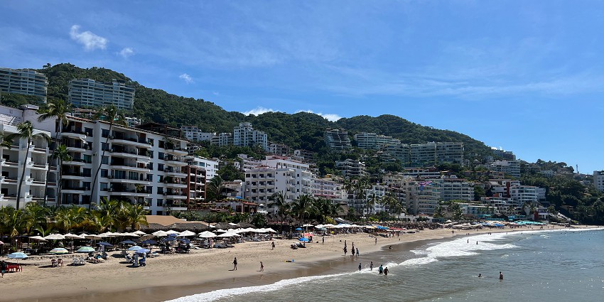 A beach scene with soft sand, calm blue ocean waves, and lush green mountains.
