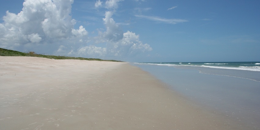 An empty Playalinda Beach boasts a blue sky with white clouds and blue waves on warm sand