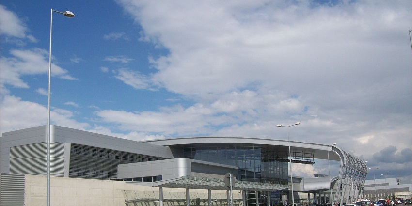 Entrance of Poznań-Ławica Henryk Wieniawski Airport with cars parked and people entering