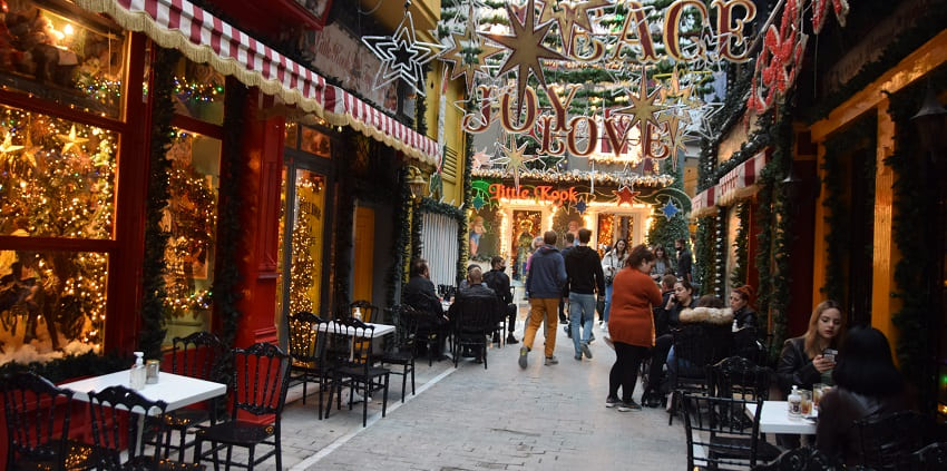Decorated street in Athens with people walking, sitting on the tables and chairs