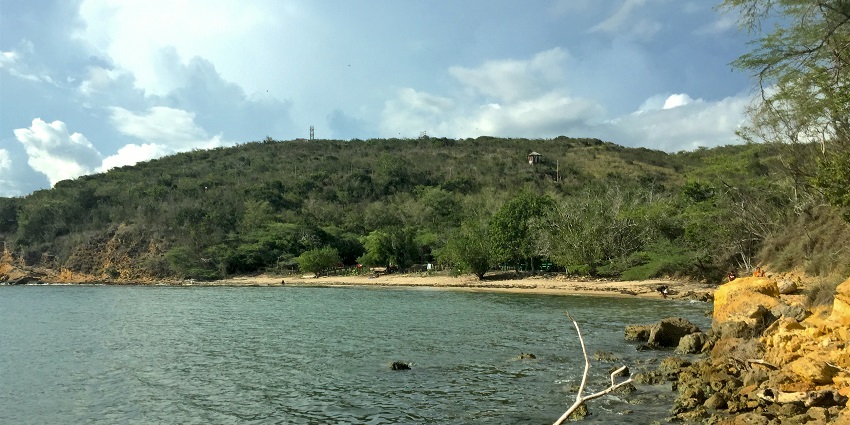 A picture of a beach with cliffs and pebbles around the shore