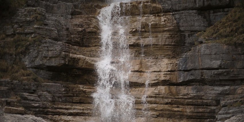 A waterfalls cascading over rocky mountains, surrounded by lush greenery and mist.
