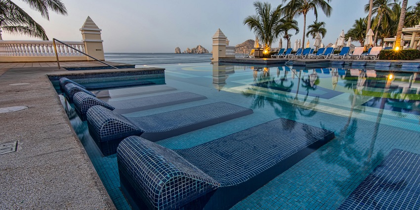 Hot water swimming pool with lounge chairs, palm trees and lights reflecting on the water