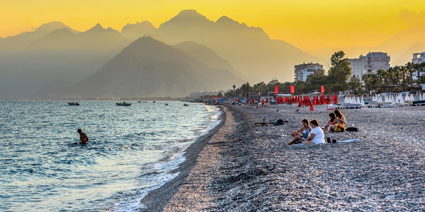 People relaxing on Konyaaltı Beach, Antalya with mountains & sunset sky background—things to do in turkey