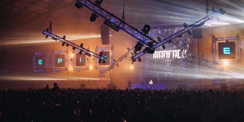 Two DJs playing the music with a crowd of people in the background holding big flags.