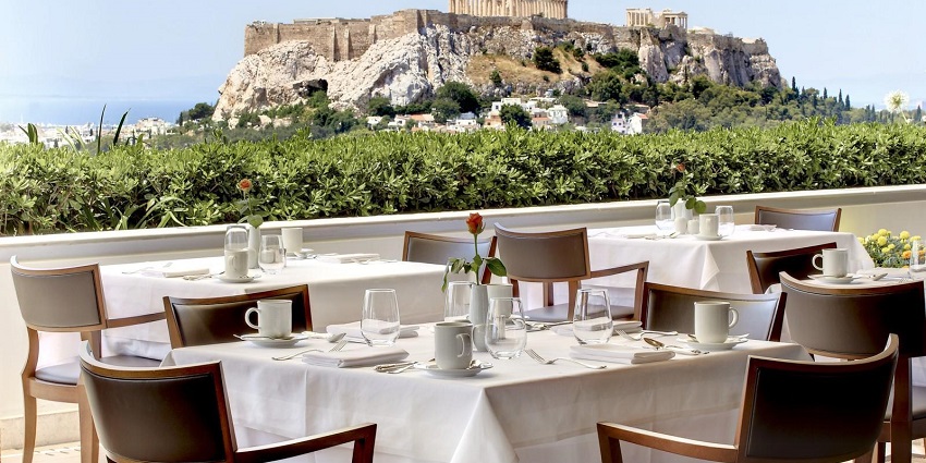 Rooftop restaurant in Athens with chairs, tables, a flowerpot, and Acropolis Hill in view