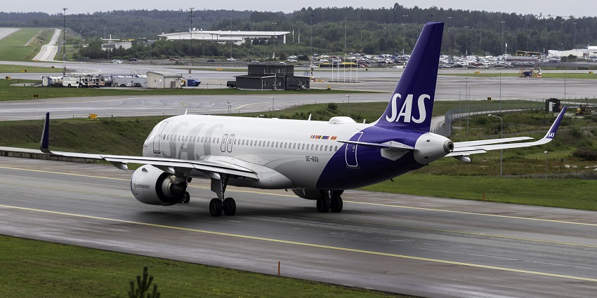 An aeroplane getting ready to take off on the runway with cars parked visible from afar.