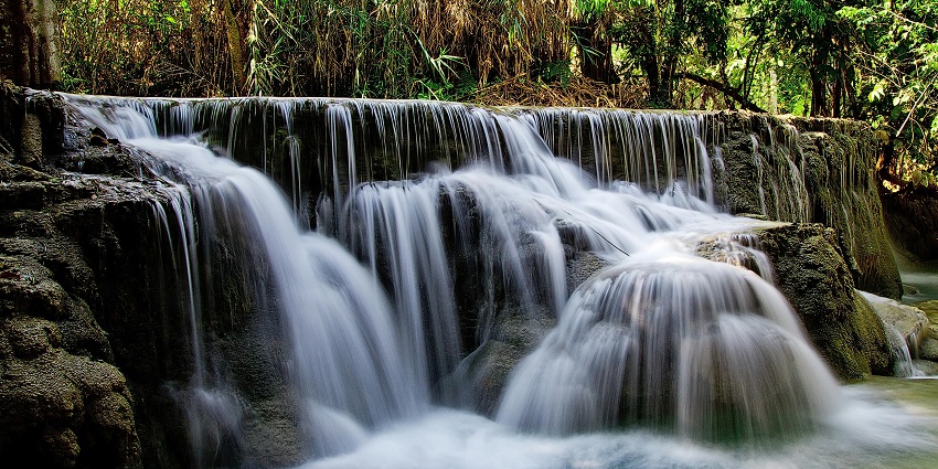 An image of a famous Waterfall in Alaska cascades beside green grass and lush vegetation