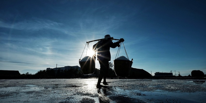 A person carrying buckets of salt during sunset, a tourist attraction near Wood Buffalo National Park.