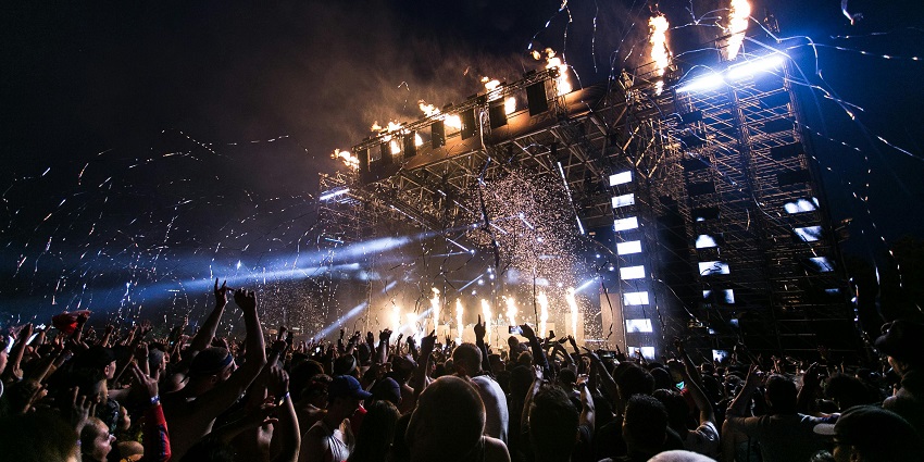 People raging and raising their hands in a concert at night with decorations and flame.