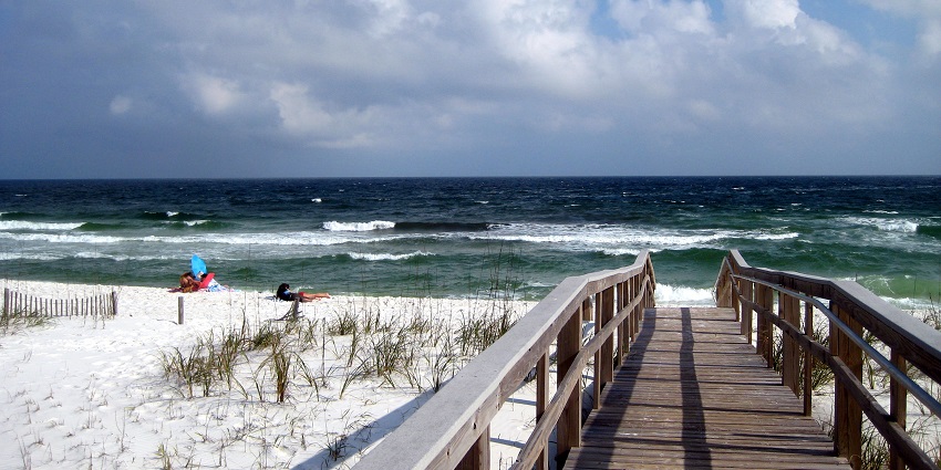 A wooden bridge on the white sand of Santa Rosa Beach leads to the blue waves of the sea