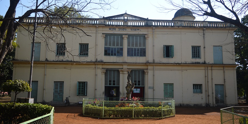 n image of Santiniketan having a dome and many window screens well enveloped with a garden.