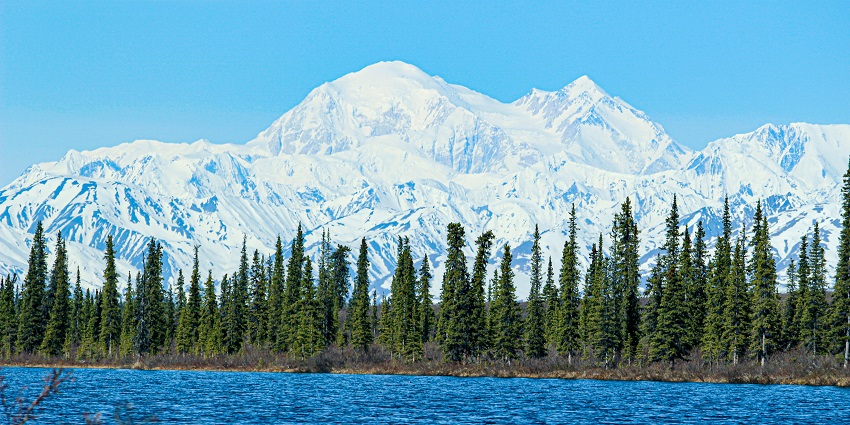 An image of the Sheldon Chalet nestled in the snow with Denali’s towering peak in the distance.