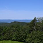 A view of Shenandoah National Park with a rocky overlook, green trees, and distant hills.