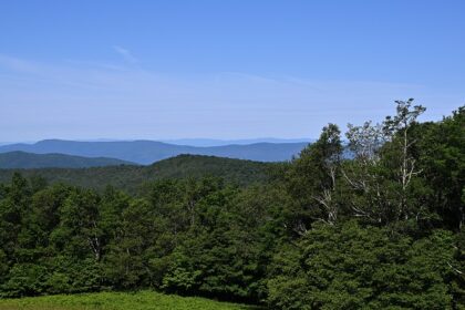 A view of Shenandoah National Park with a rocky overlook, green trees, and distant hills.