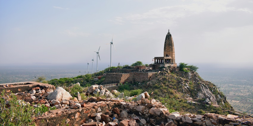 A distant view of a Hindu temple at a cliff end, with views of the city in the background