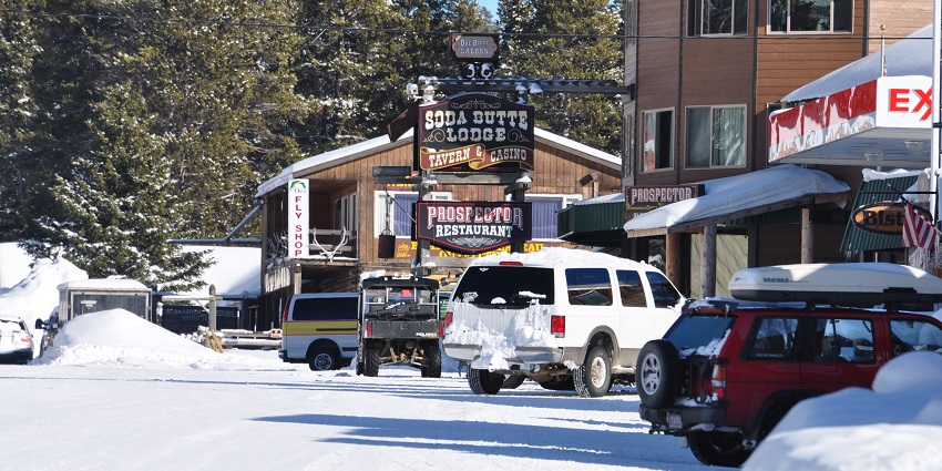 A serene winter scene in Cooke City, Montana, with snow-covered buildings and streets.
