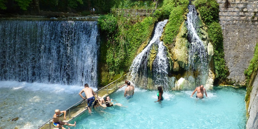 Springs of Loutraki with small waterfalls and multiple people enjoying the spring pond.
