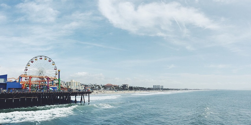 Santa Monica beach and pier with a Ferris wheel, a roller coaster track and distant people