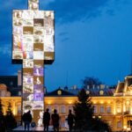 People standing near a monument and a palace at night with graffiti on the wall.