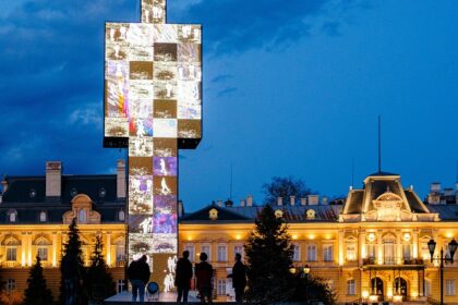 People standing near a monument and a palace at night with graffiti on the wall.