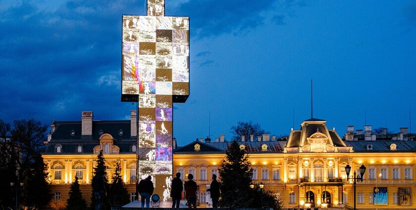 People standing near a monument and a palace at night with graffiti on the wall.