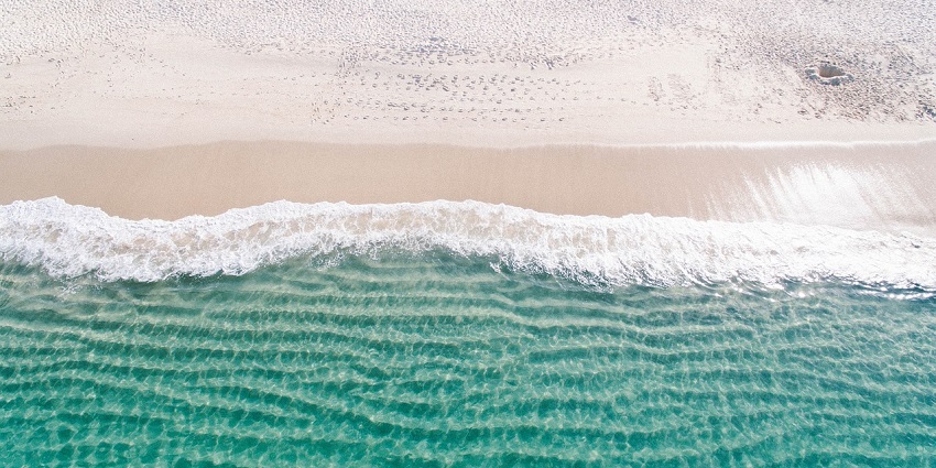An aerial shot of a beach with white sand and clear turquoise water lapping at the shore